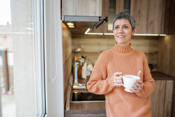 istock Mature woman in the kitchen drinking her morning coffee while looking through the window 2135283959