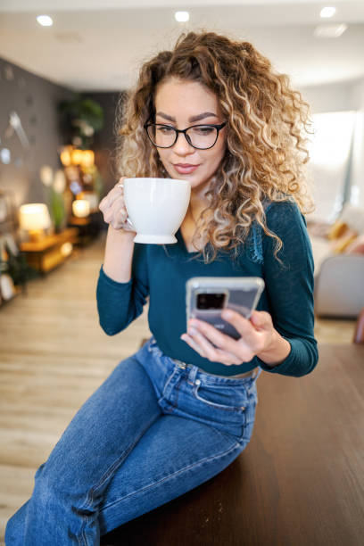 istock Young woman drinking her coffee and using mobile phone at home 2135299075