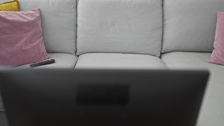 Middle-aged woman sitting on a couch in a cozy living room using a smartphone and remote control