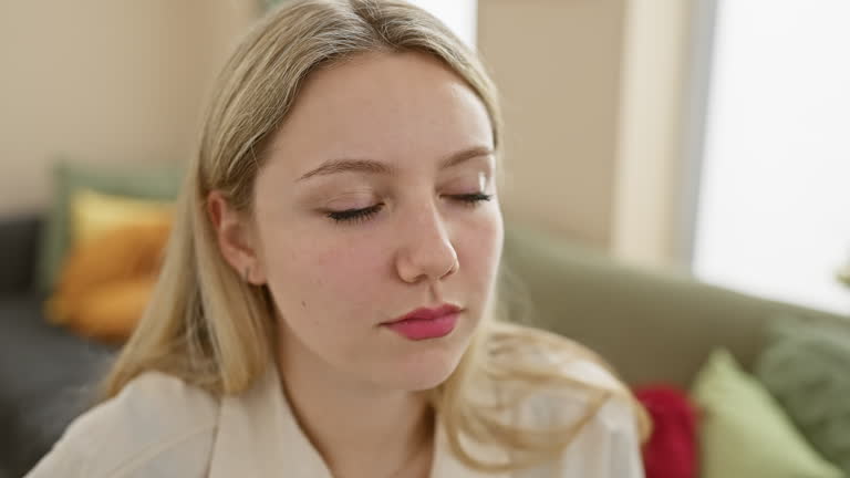 A contemplative young woman sits in a comfortable living room, her expression pensive and serene.