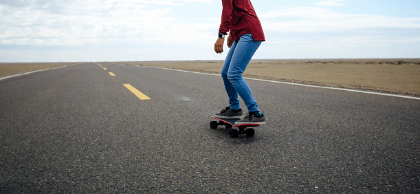 Asian woman skateboarder skateboarding on trail cross the desert