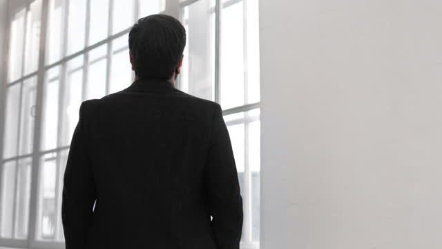 Pensive male business person in classical suit looking at windows of office building, back view