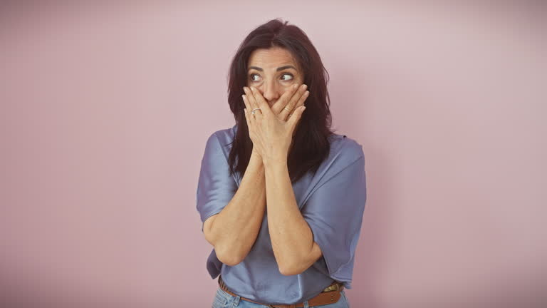 Stunned middle-aged hispanic woman covers mouth in shock, realizing her mistake! captured over an isolated pink background in a moment of astonished silence.