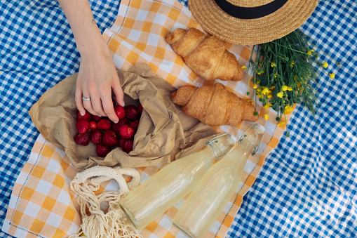 Delightful picnic: croissants, strawberries, lemonade on checkered blanket.