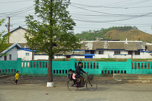 Wonsan, North Korea - May 4, 2019: Street scene in Wonsan. Local man carrying children on a bicycle