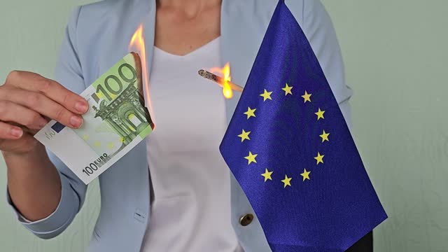 Burning euro banknotes in hands and flag. 100 euro banknotes and inflation in the European Union concept