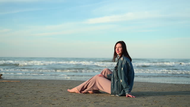 mid adult woman sitting on a beach in a springtime sunset.