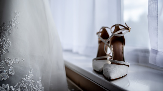 Bride's White Wedding Shoes on Window Sill next to Wedding Dress