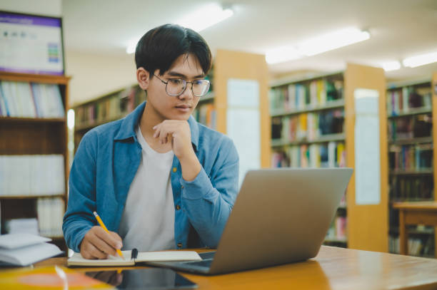 istock Male college students are working on laptops and searching for books to study, make reports, find useful information in college room. Concept of reading, learning and intelligence. 2135466578