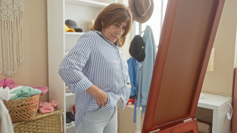 Mature woman dressing in a tidy room with mirror, wardrobe, and casual attire reflecting personal style and comfort.