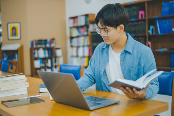 istock Male college students are working on laptops and searching for books to study, make reports, find useful information in college room. Concept of reading, learning and intelligence. 2135469308