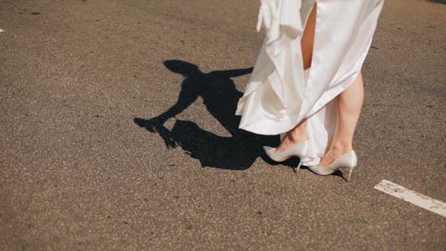 A girl walks in a dress in the center of the road with her arms spread. Her shadow falls beautifully on the asphalt