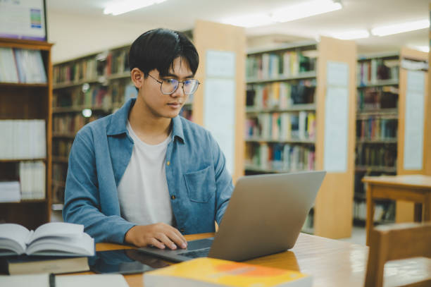 istock Male college students are working on laptops and searching for books to study, make reports, find useful information in college room. Concept of reading, learning and intelligence. 2135470371