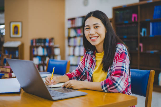 istock Smiling female student posing while working on laptop and searching for books to study, make report, find useful information in university room. 2135474082