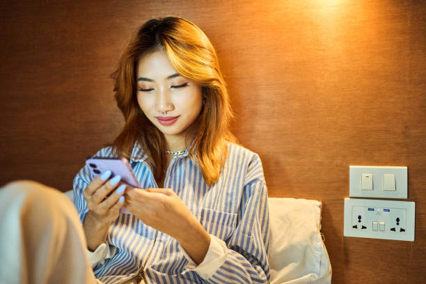 Smiling young woman using her phone in her hostel dorm bed