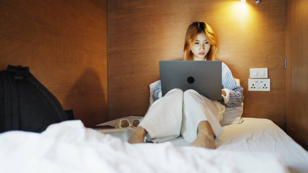 istock Young woman sitting on her hostel dorm bed and working on a laptop 2135476757