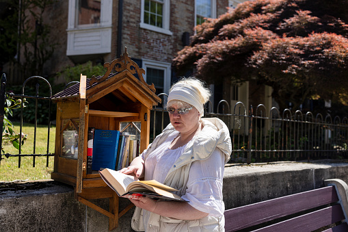 Literary exchange on the spring streets: mature woman collects books from a house-shaped wooden container in Jim Thorpe, Pennsylvania