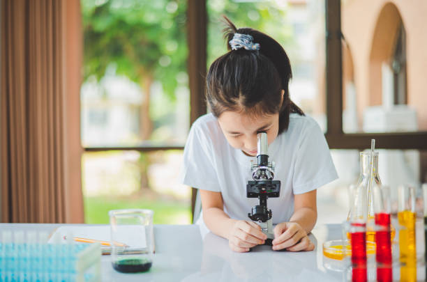 istock little scientist looking through a microscope and test tubes filled with chemicals for learning about science and experiments. 2135478919