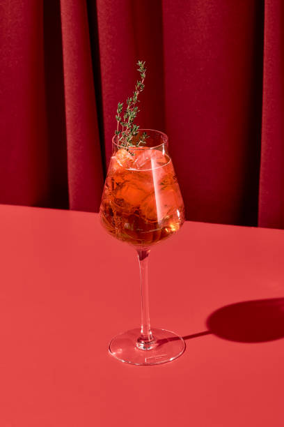 alcohol cocktail with aperol and thyme on red background with shadow. spritz cocktail on coloured background in trendy style. contemporary concept with alcohol beverage. bartender cocktail. - cocktailfeest-fotos stockfoto's en -beelden