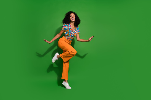 Full body length size photo of funny positive girl curly chevelure dancing in rhythm with music isolated over green color background.