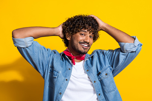 Photo portrait of attractive young man touch hair hairstyle dressed stylish denim clothes red scarf isolated on yellow color background.