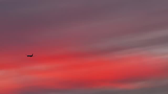 large cargo plane flying through bright pink fluffy clouds at sunset telephoto aerial