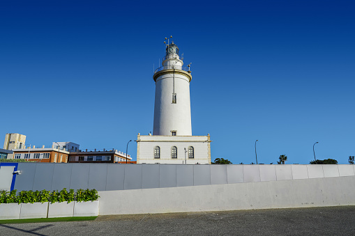 White lighthouse protecting the harbor in Malaga Spain on a bright sunny day with a blue sky