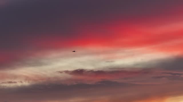 large cargo plane flying through bright pink fluffy clouds at sunset STATIC AERIAL TELEPHOTO