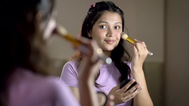 Beautiful happy young woman applying blush on cheeks with brush front of the mirror.
