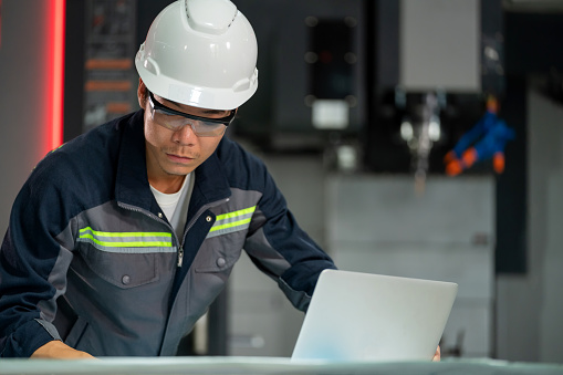 Dedicated engineers, clad in reflective safety gear, is depicted actively using laptop to analyze market data aimed at boosting production efficiency. Collaborative expertise and technological integration as the team engages in discussions focused on maximizing efficiency in the industrial setting.