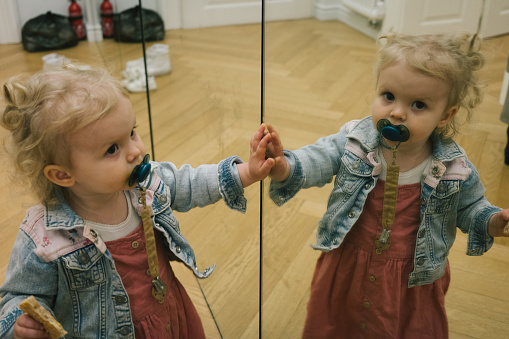 Toddler looks at self in mirror while eating