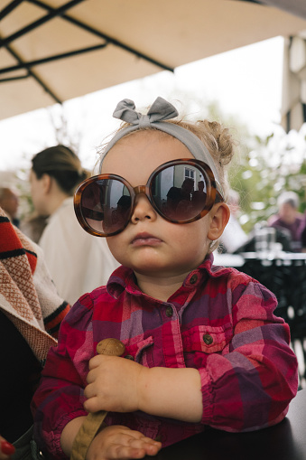 Toddler relaxes in outdoor cafe and plays with sunglasses
