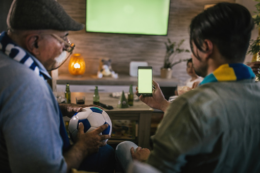 group of people watching soccer match at home and using smart phone for sports betting