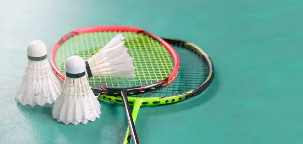 Photo of White badminton shuttlecocks and badminton rackets on green floor indoor badminton court soft and selective focus on shuttlecocks and the rackets