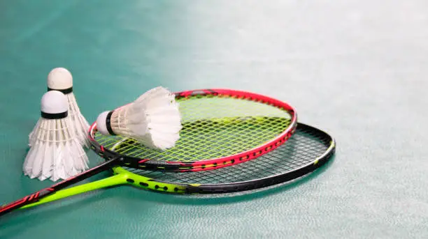 Photo of White badminton shuttlecocks and badminton rackets on green floor indoor badminton court soft and selective focus on shuttlecocks and the rackets