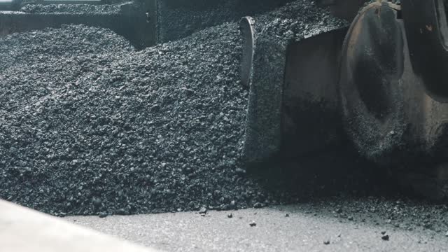 Pavement machine laying fresh asphalt during highway construction