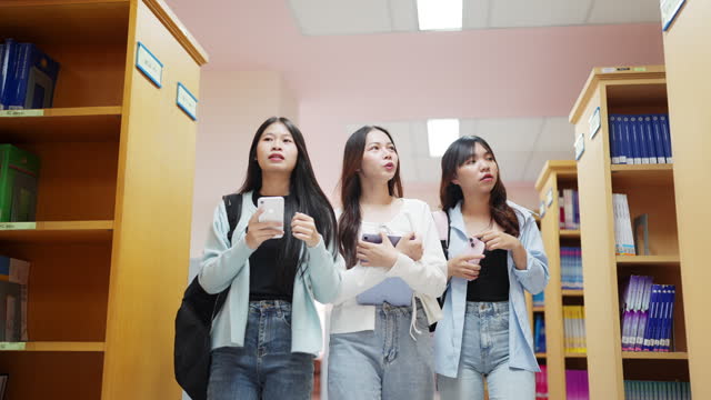 Three women are walking down a hallway with their cell phones in their hands