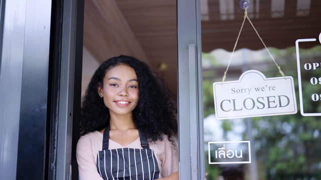 Happy young woman in an apron turned the closed sign to open the front door.