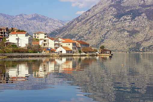 Beautiful Mediterranean landscape on sunny spring day. Montenegro, Adriatic Sea.View of Kotor Bay and Prcanj town. Mountains and town reflect in water