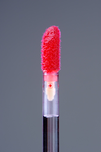 Vibrant scarlet hue of a lip gloss applicator against a grey background, capturing its glossy texture and luxurious allure, perfect for beauty and cosmetic-themed projects.