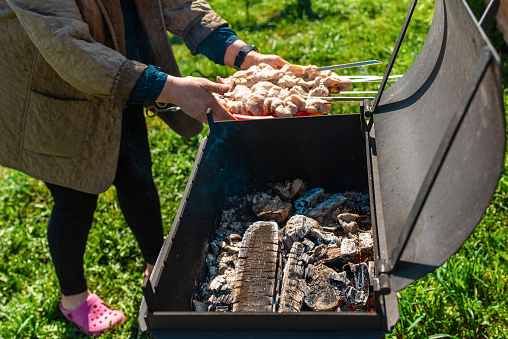 Woman strands raw pieces of marinatedo pork meat on long skewers frying shish on the grill.Nice summer day.