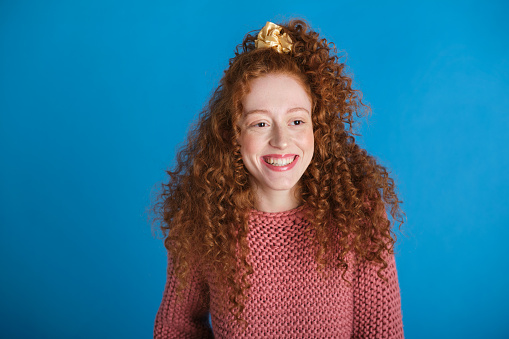 medium shot portrait of a carefree generation z white woman with redhead pigtail and big smile in a blue background studio
