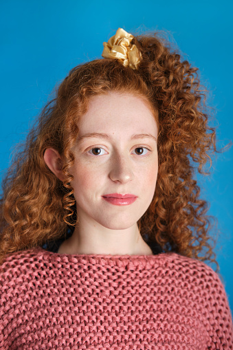 medium shot portrait of a carefree generation z white woman with redhead  pigtail and big smile and a pink sweeter in a blue background studio