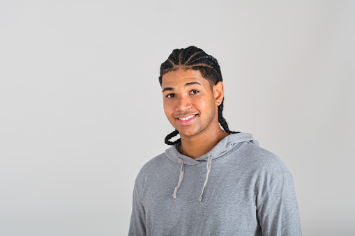 front view portrait of a confident young Dominican man with a gray hoodie and big smile in a white studio background
