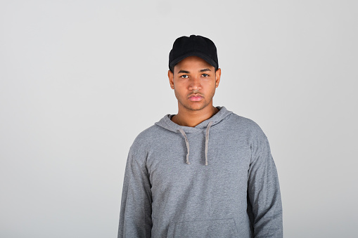 front view portrait of a confident young Dominican man with a cap and a gray hoodie in a white studio background