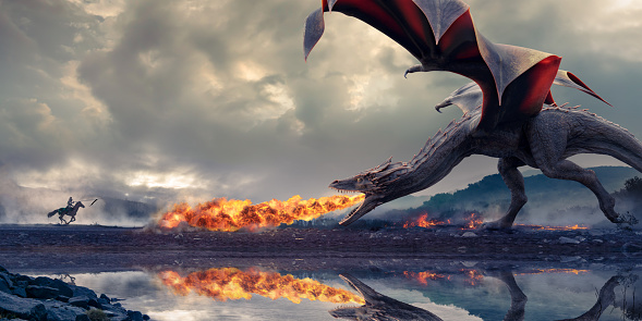 A knight wearing full armour rides on horseback towards a huge dragon with wings out and head lowered, breathing fire under a dramatic cloudy sky beside the edge of a lake.