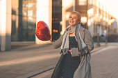 middle-aged happy woman with a heart-shaped balloon falling a love, having a fun day, walking around English city Spring is in the air Lifestyle, tourism, valentines day, world woman's day concept