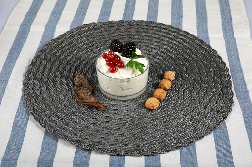 Cottage cheese cream in glass cup with currants and blackberries on a gray wicker circle
