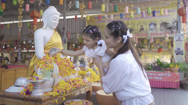Thai mother and daughter bathe Buddha image during Songkran festival in Thailand.