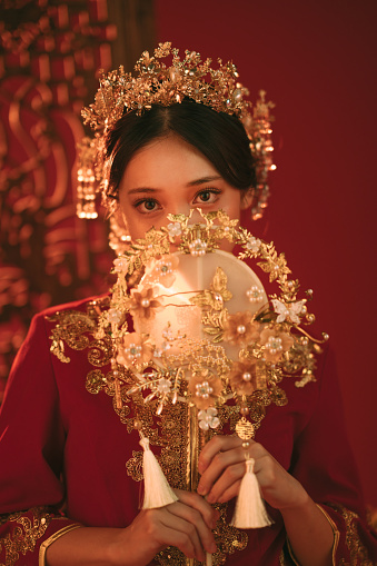 Stunning Asian Chinese woman in traditional bridal tea dress and headwear against a red background